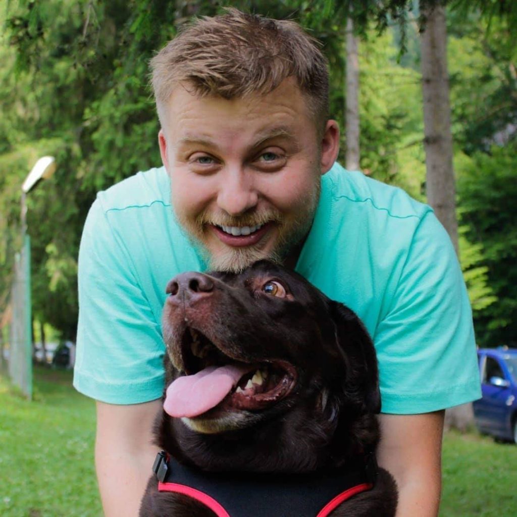 A young man in a green t-shirt is smiling while petting a black dog