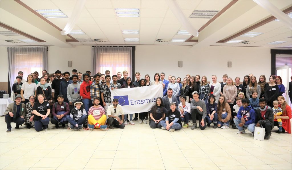 A group of young people are posing around the Erasmus+ flag
